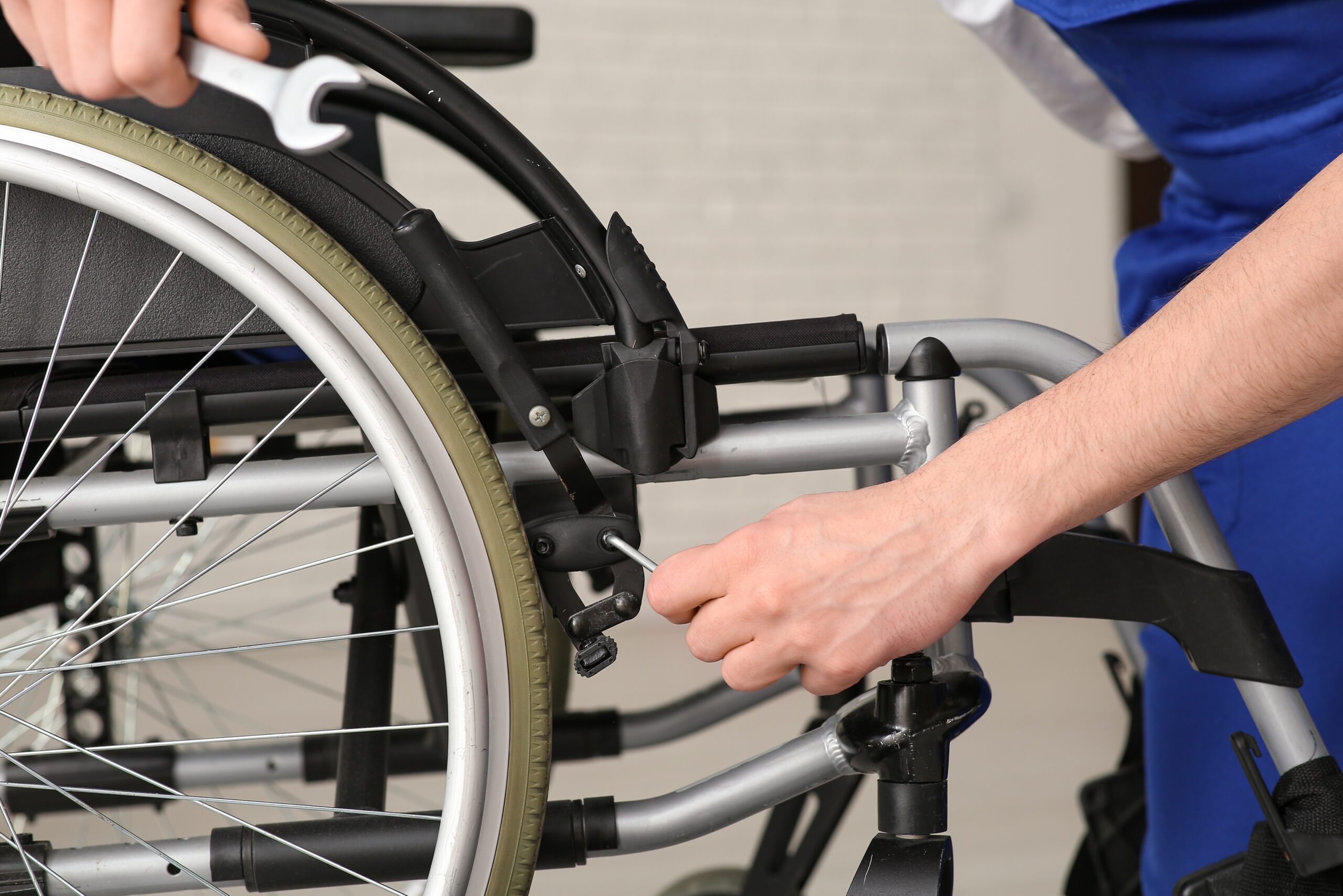 Close-up of hands adjusting a wheelchair, focusing on the rear wheel and frame.