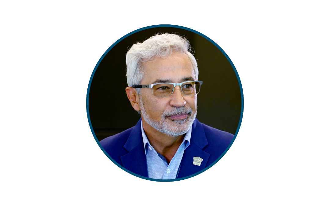 Portrait of a middle-aged man with gray hair and glasses wearing a blue blazer and light blue shirt, facing slightly to the right.